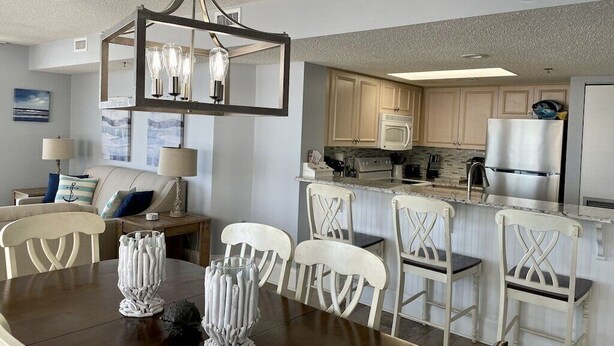 A modern kitchen with white cabinetry, a central island, and a dining area with a wooden table and white chairs.
