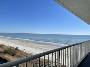 A beach view from a balcony with a railing, a clear sky, and the ocean.