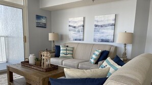 A living room with a beige sofa, a wooden coffee table, and a lamp. There are three wall-mounted paintings above the sofa.