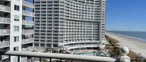 A high-rise hotel with multiple balconies, a pool, and a beach view.
