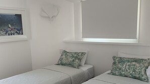 Un dormitorio con dos camas individuales, una ventana con vista a barcos y una lámpara fijada a la pared.