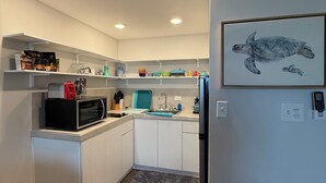 Een moderne keuken met witte kasten, een magnetron, een spoelbak en een kunstwerk van een zeeschildpad aan de muur.
