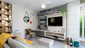Ein modernes Wohnzimmer mit einer Couch, einem Sessel, einem an einer Holzwand befestigten Fernseher und einer kleinen Pflanze.