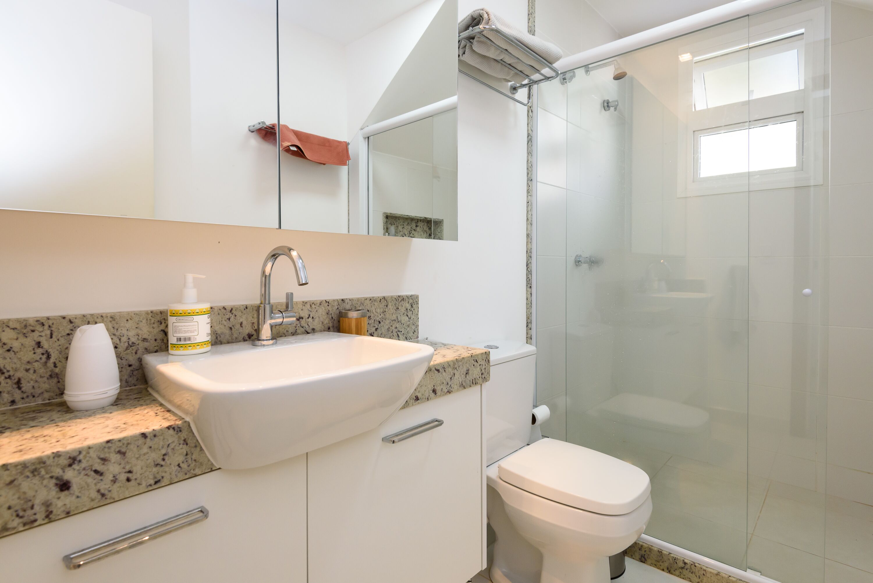 A modern bathroom with a granite countertop, a white sink, a mirror, a glass shower enclosure, and a toilet.