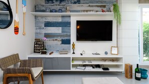 Ein modernes Wohnzimmer mit Flachbildfernseher, Holzmöbeln, Dekoration und Blick ins Freie.