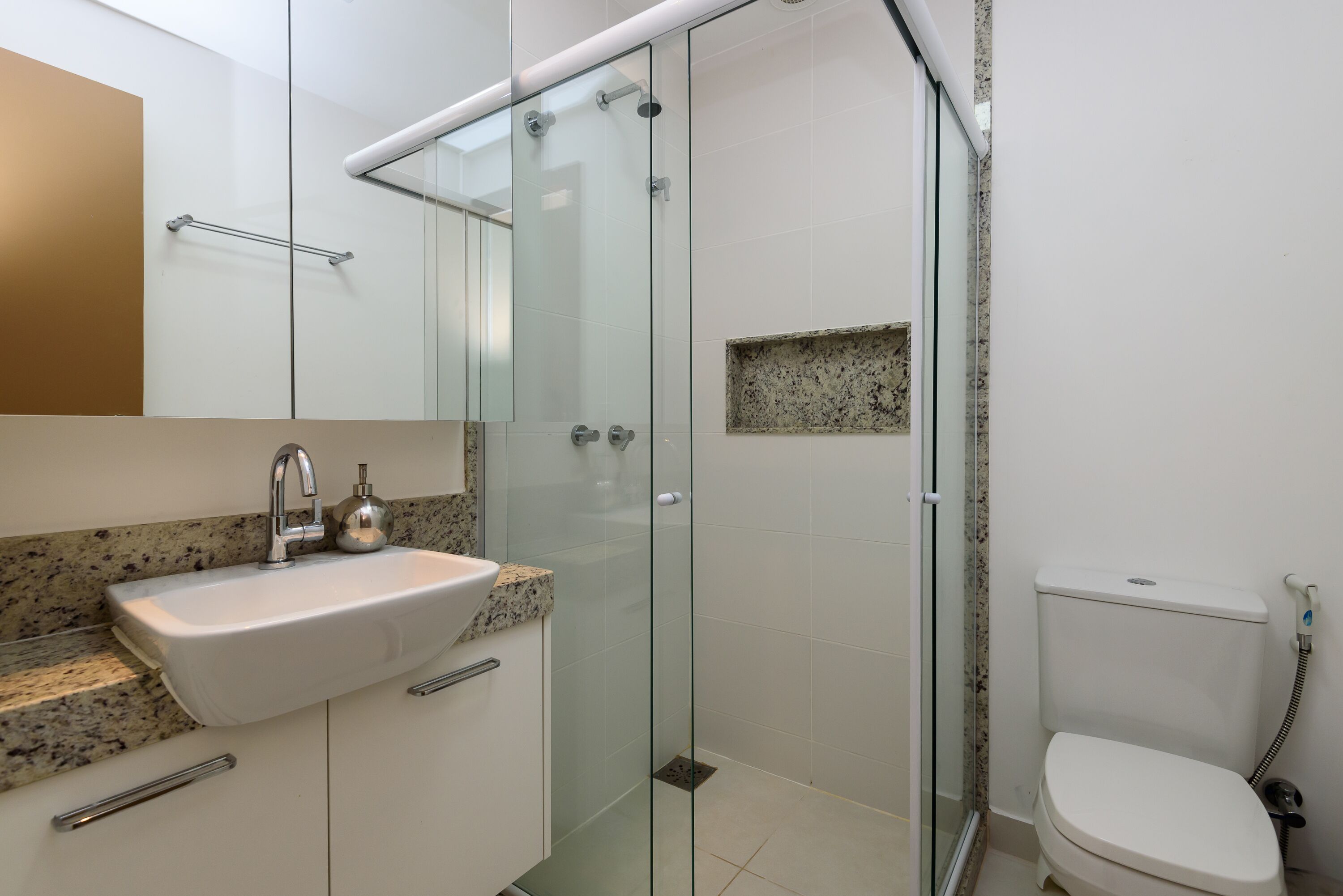 A modern bathroom with a glass-enclosed shower, a white sink with a granite countertop, and a toilet with a bidet attachment.