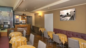 A restaurant with round tables covered in yellow tablecloths, a counter with a coffee machine, and a painting of a racing car on the wall. - Hotel Il Giardino (Pisa)