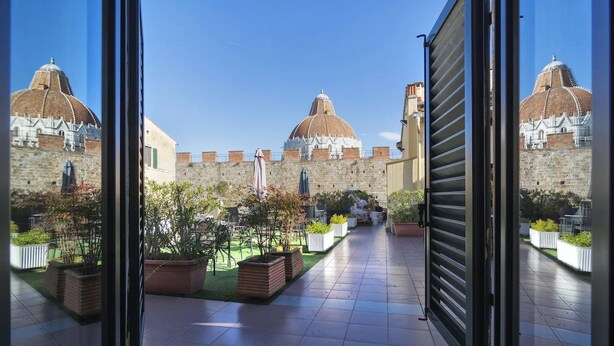 A courtyard with a tiled floor, potted plants, and a view of a historic building with domed roofs. - Hotel Il Giardino (Pisa)