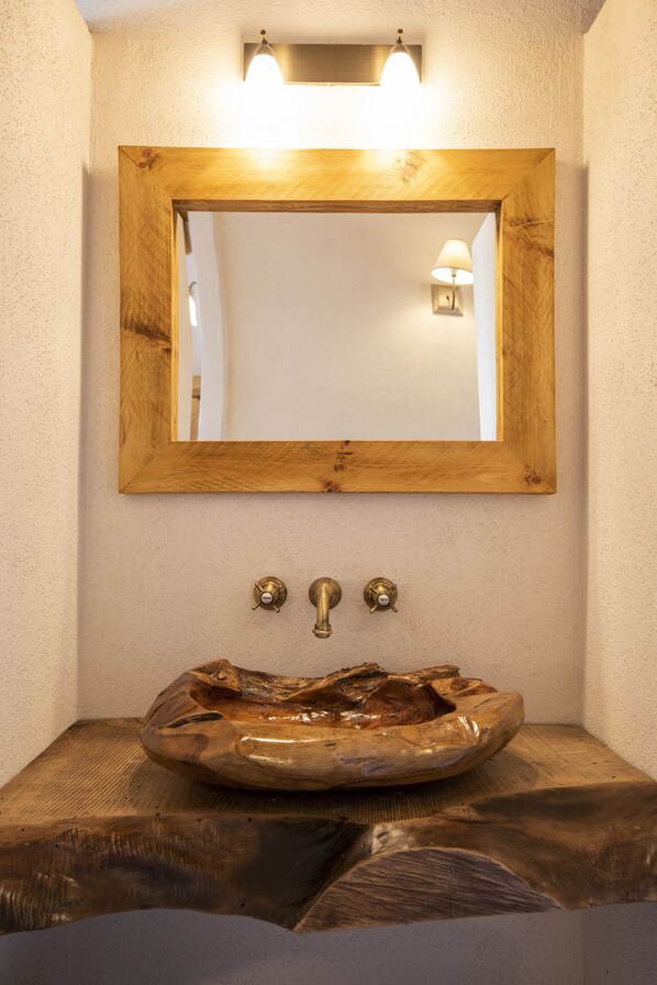A bathroom with a wooden-framed mirror, a wooden basin, and two brass fixtures.