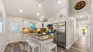 A modern kitchen with white cabinetry, stainless steel appliances, and a central island with bar stools.