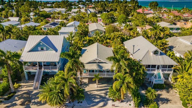 A coastal residential area with houses featuring gabled roofs and balconies, surrounded by palm trees and a clear view of the ocean.
