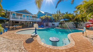 A backyard with a swimming pool, patio furniture, and a house with a balcony.