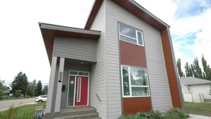Une maison moderne à deux étages, avec une porte rouge, un petit porche et une pelouse bien entretenue.