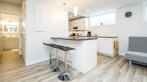 Une cuisine moderne avec des meubles blancs, un îlot central doté de tabourets, un four à micro-ondes et une machine à café.