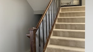 Una escalera alfombrada con barandillas de madera y un zócalo de madera oscura.