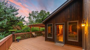 A wooden deck with outdoor seating, a covered area with string lights, and a building with large windows and a door.