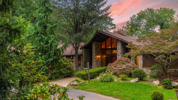 A stone house with a sloped roof, surrounded by lush greenery and a well-maintained lawn.