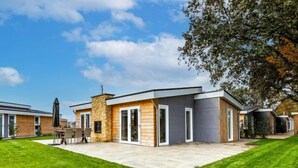 A modern house with a stone chimney, a patio with outdoor furniture, and a well-maintained lawn.