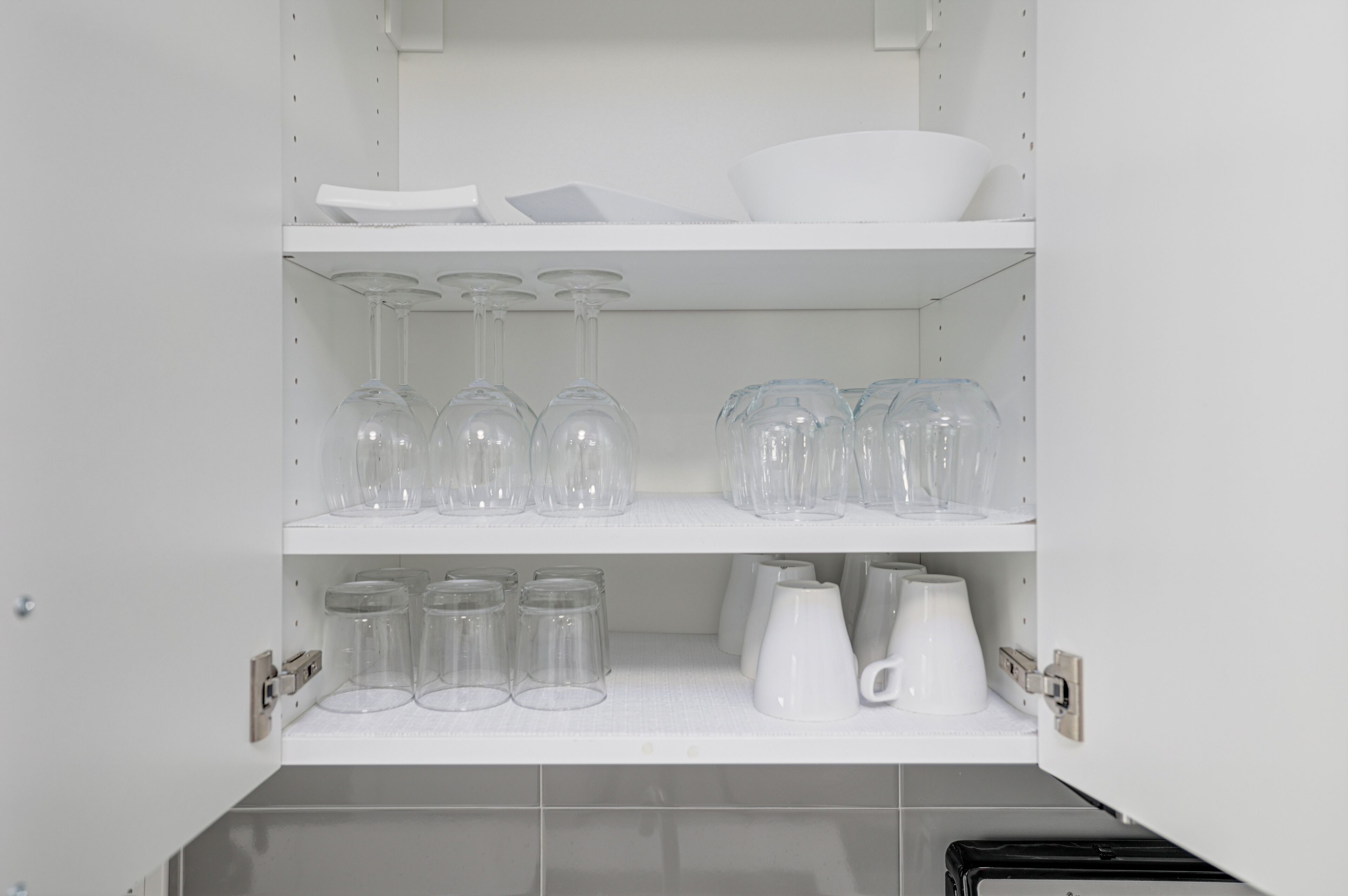 A white shelf unit with clear glassware, white mugs, and a white pitcher.