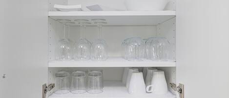 A white shelf unit with clear glassware, white mugs, and a white pitcher.