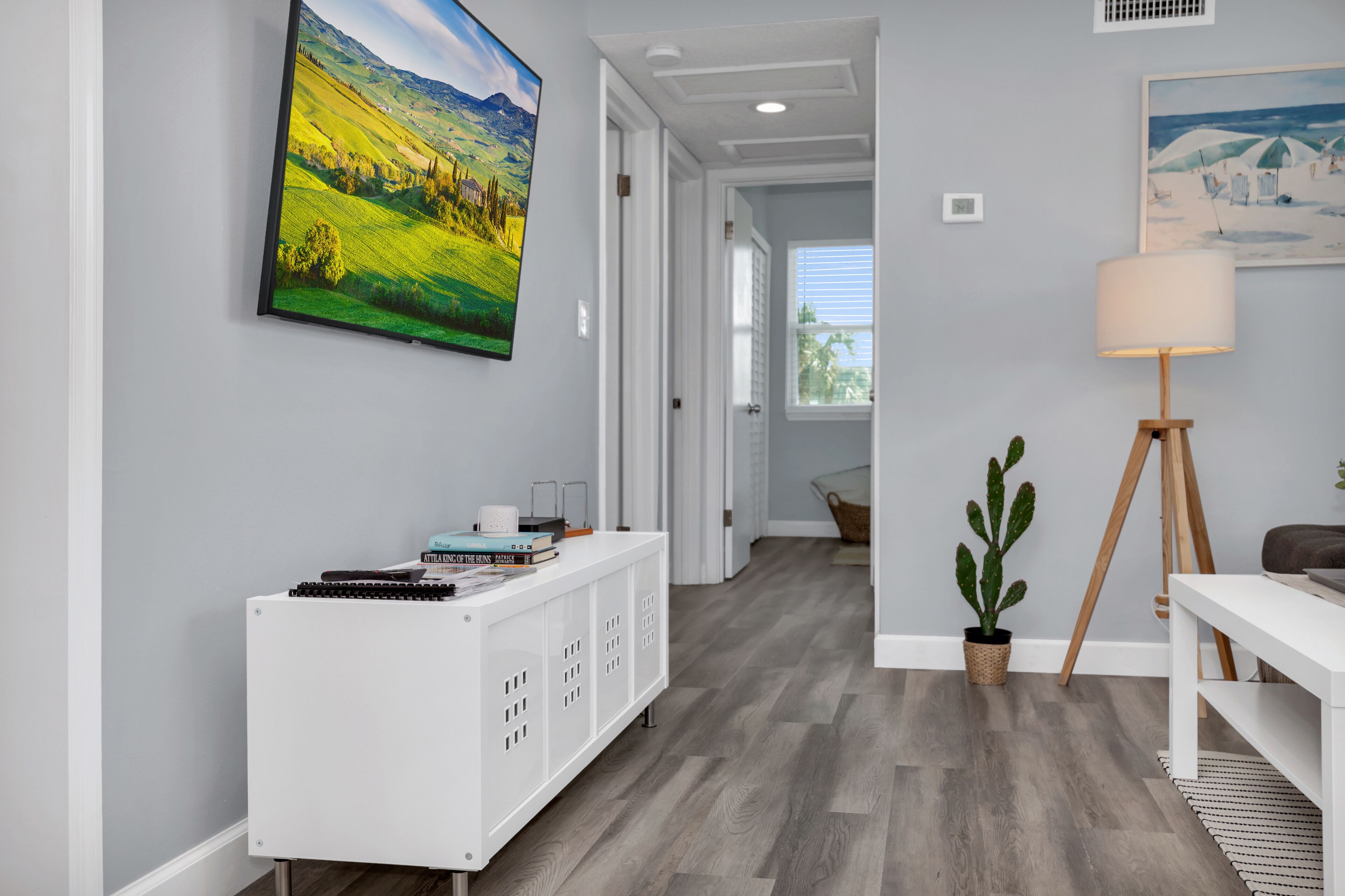 Un interior moderno con una consola blanca, una planta de cactus y un cuadro de un paisaje.