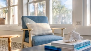 A room with a blue armchair, a wooden side table, and a book titled "SURF JAHUA" on a coffee table. - 1 minute to beach 6 BR 5 baths private heated pool Games Sleeps 2-19 (Panama City Beach)