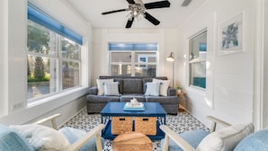 A sunlit room with a ceiling fan, a gray sofa with white cushions, a blue coffee table, and a patterned floor. - 1 minute to beach 6 BR 5 baths private heated pool Games Sleeps 2-19 (Panama City Beach)