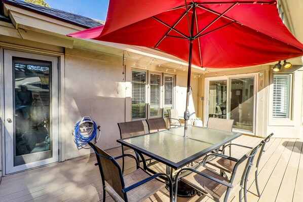 An outdoor patio with a glass table and chairs, a red umbrella, and a hose coiled on the wall.