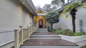 A staircase leading to a house entrance with a wooden handrail, a door with a glass panel, and a small garden with a palm tree and decorative metalwork. - Sunset Rentals | Kingston Dunes 80 (Hilton Head Island)