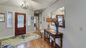 A hallway with a wooden floor, a blue and yellow rug, a wooden bench, a table with a vase, and a chandelier. - Sunset Rentals | Kingston Dunes 80 (Hilton Head Island)