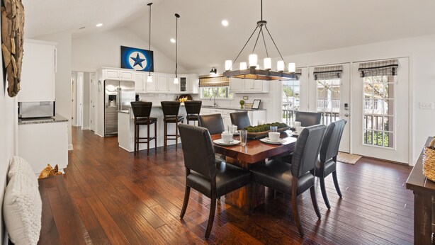 A spacious kitchen with white cabinets, a central island, and a dining area with a wooden table and chairs. - Blue Star Bungalow steps to the Beach with Heated Pool, sleeps 8 (Saint Simons Island)