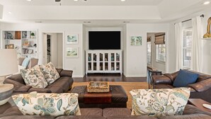 A modern living room with leather sofas, a flat-screen TV, and a ceiling fan. - Blue Star Bungalow steps to the Beach with Heated Pool, sleeps 8 (Saint Simons Island)