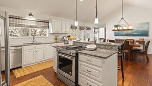 A modern kitchen with white cabinets, a granite countertop, a built-in oven, and a dining area with a wooden table and chairs. - Blue Star Bungalow steps to the Beach with Heated Pool, sleeps 8 (Saint Simons Island)