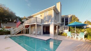 A two-story house with a swimming pool, outdoor seating, and an American flag. - Blue Star Bungalow steps to the Beach with Heated Pool, sleeps 8 (Saint Simons Island)