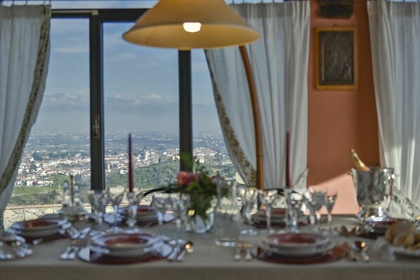 Une table à manger dressée avec des assiettes, des verres et des couverts, offrant une vue sur le paysage urbain à travers de grandes fenêtres.