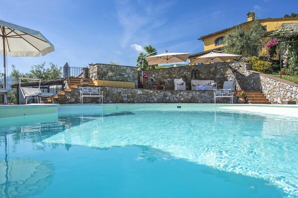 A swimming pool with stone walls, outdoor seating, and a clear blue sky.