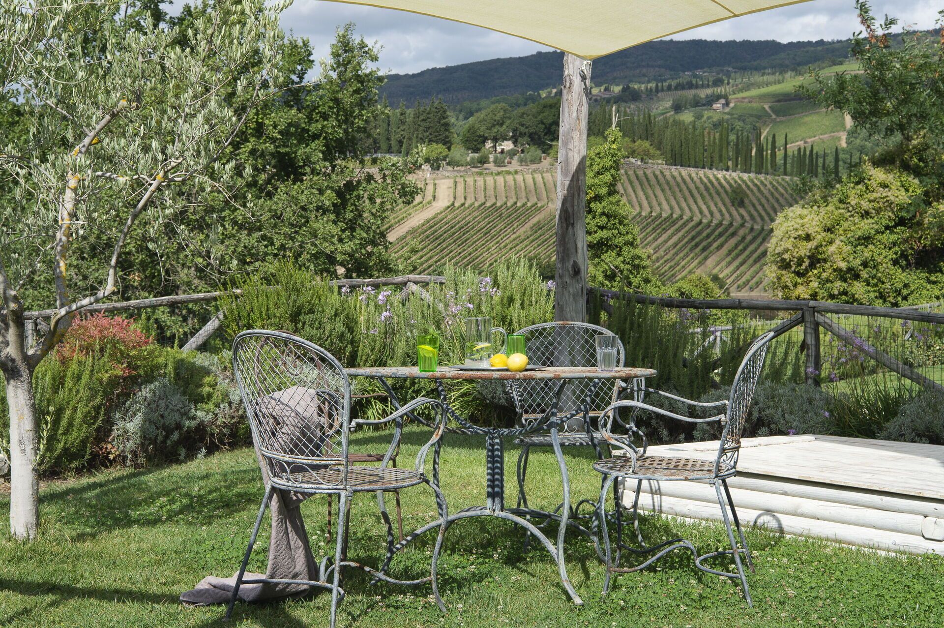 A rustic outdoor seating area with metal chairs and a table, overlooking a vineyard and rolling hills.