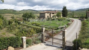 Uma propriedade rural com casa de pedra, acesso por caminho de cascalho e vinhedos ao redor.