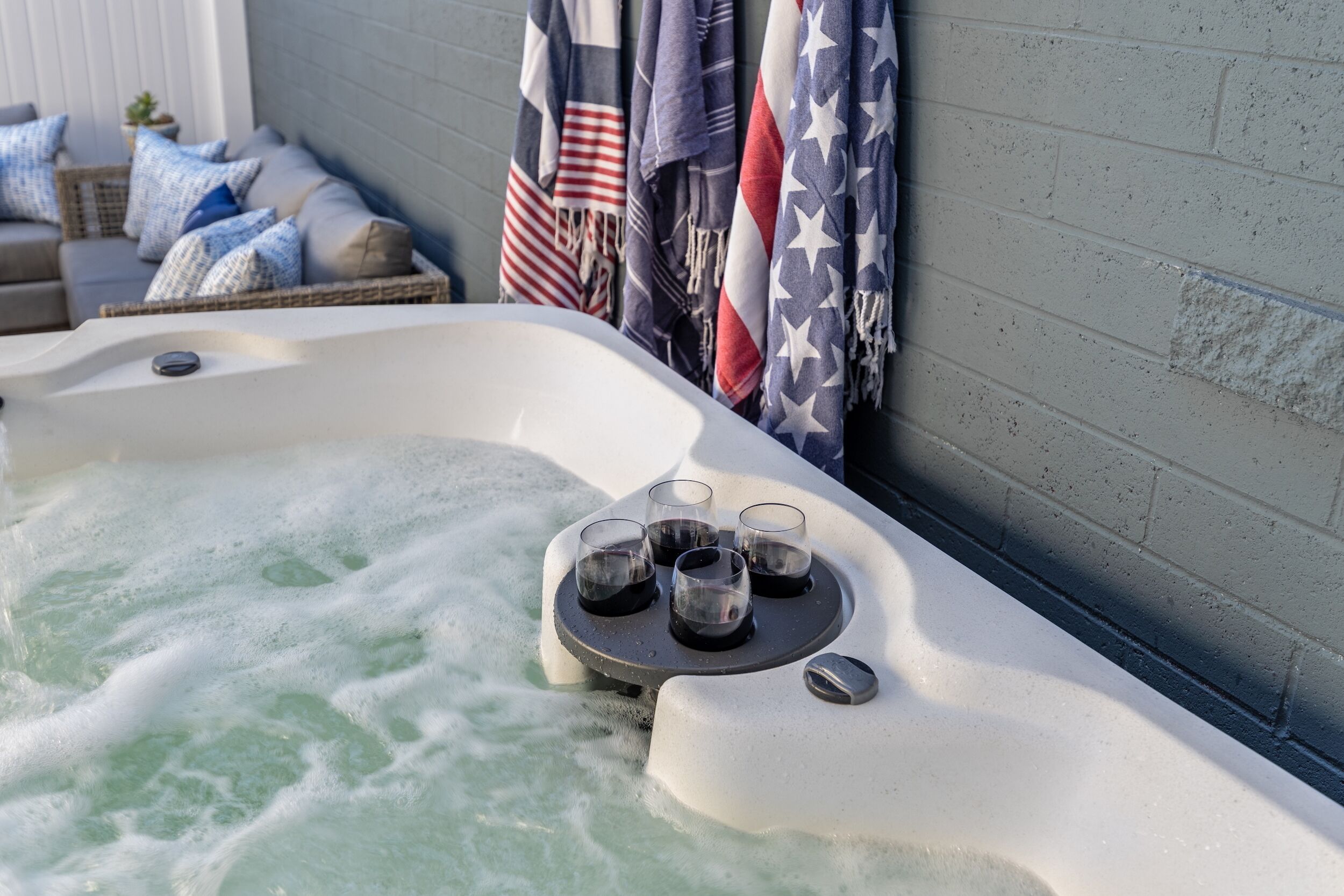 A hot tub with four glasses of water, a brick wall, and American flags.