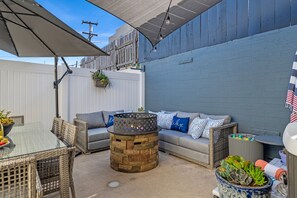 An outdoor patio area with a glass-top table, wicker chairs, a stone fire pit, and a gray sofa with patterned cushions. - HOT TUB, Parking, A/C - Near SeaWorld, Beaches, MCRD, Barnes Tennis, PLNU! (San Diego)