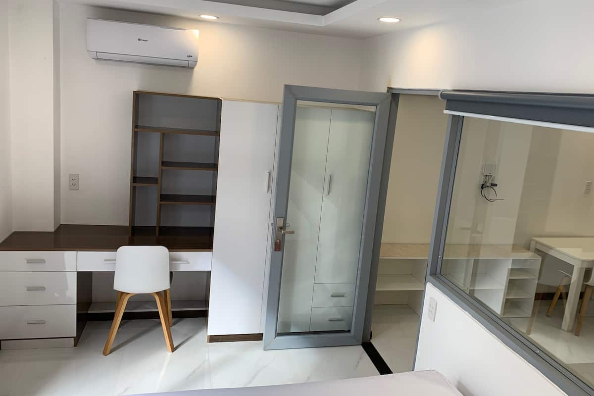 Quarto moderno com escrivaninha, cadeira, guarda-roupa e porta de vidro para um banheiro.