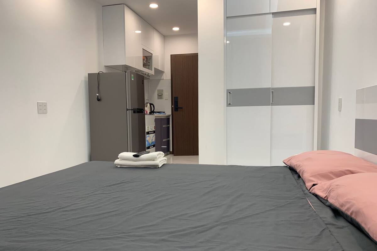 Quarto de hotel moderno com cama, guarda-roupa, kitchenette e casa de banho.