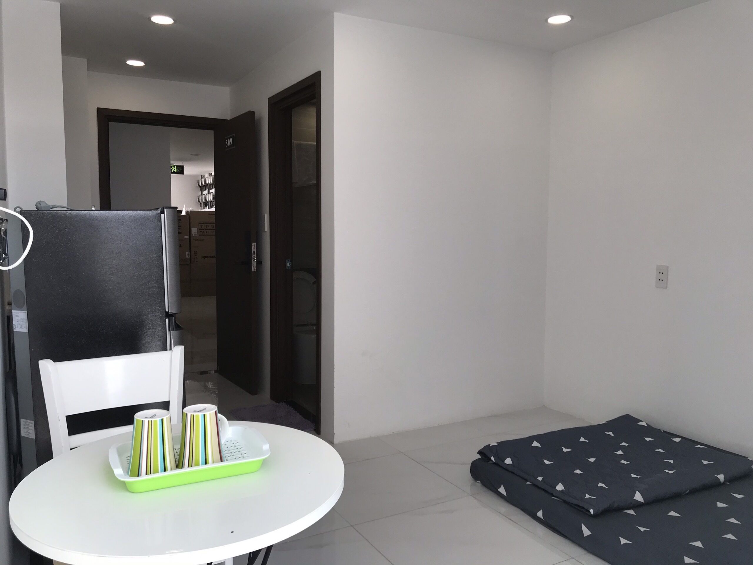 A small, modern room with a white table, a black sofa, and a door leading to a kitchen.