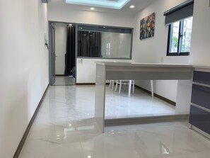 A modern kitchen with a white countertop, a dining area with a white table and chairs, and a large window with a view of the outdoors.