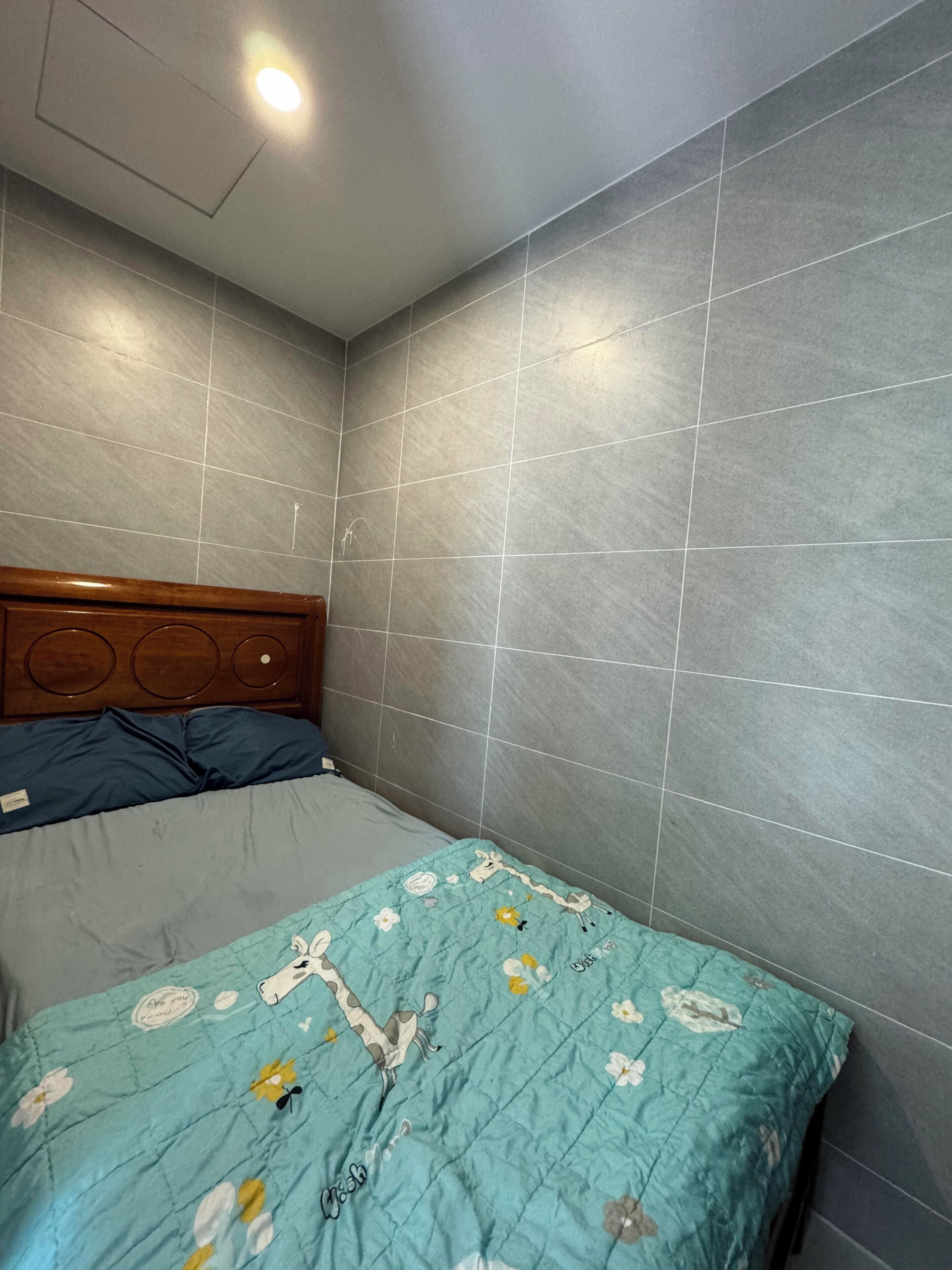 A room with a bed, grey tiled walls, and a wooden headboard.