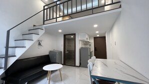 Un appartement moderne comprenant un escalier, un espace de vie avec un canapé et une petite table ronde, une cuisine équipée d’un réfrigérateur et de placards, et une salle de bain avec douche.