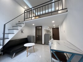 Un apartamento moderno con una escalera, una sala de estar con sofá y una mesa redonda pequeña, una cocina con refrigerador y armarios, y un baño con ducha.