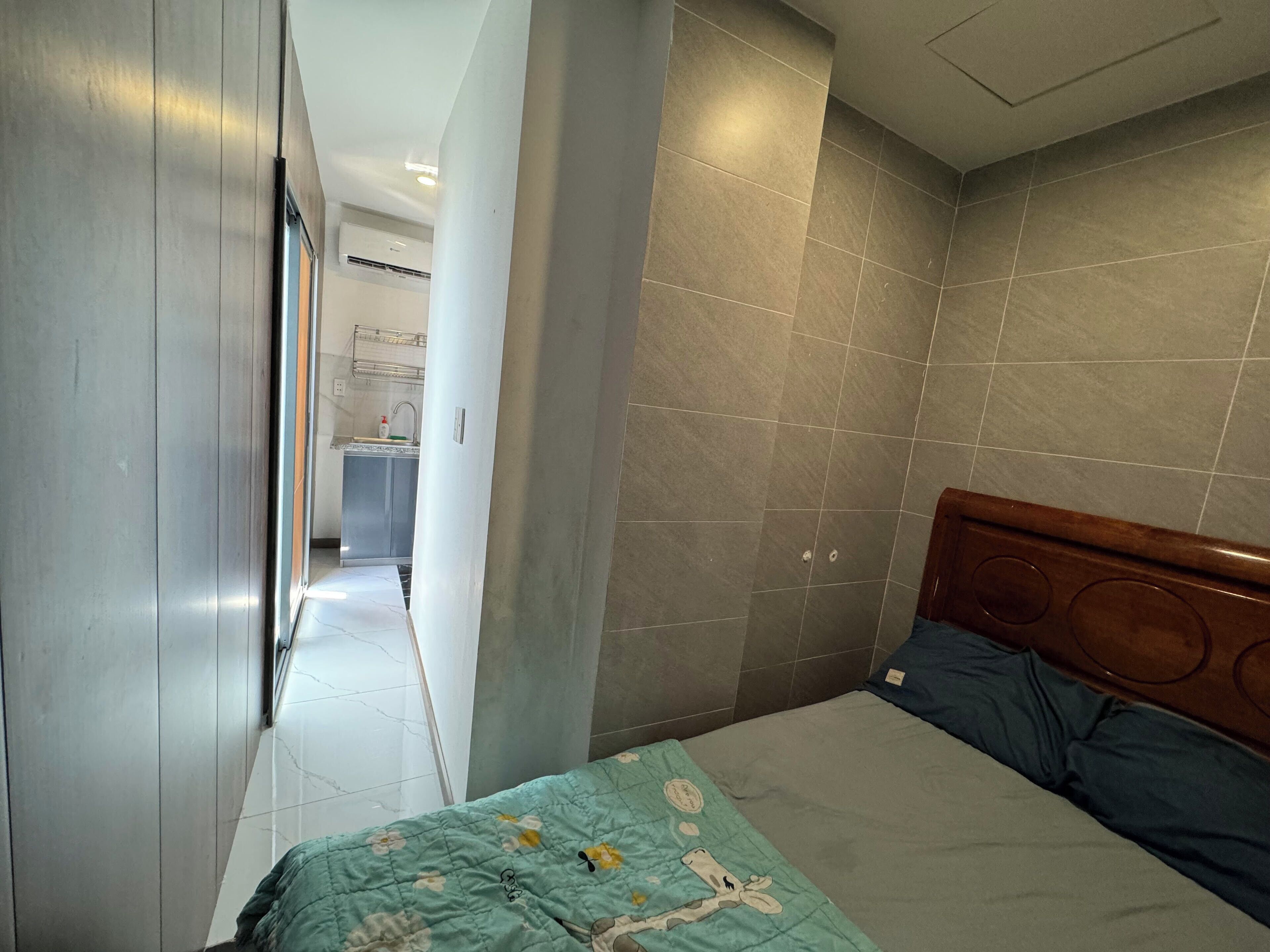 A bedroom with a bed, a wooden headboard, and a bathroom visible in the background.
