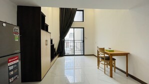 Une petite pièce propre, dotée d’une kitchenette, d’un coin repas avec une table et des chaises, et d’une grande fenêtre avec des rideaux.