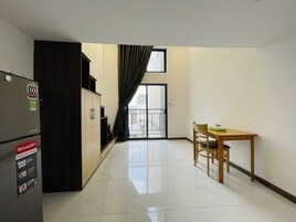 Una habitación pequeña y limpia con kitchenette, un comedor con mesa y sillas, y un ventanal con cortinas.